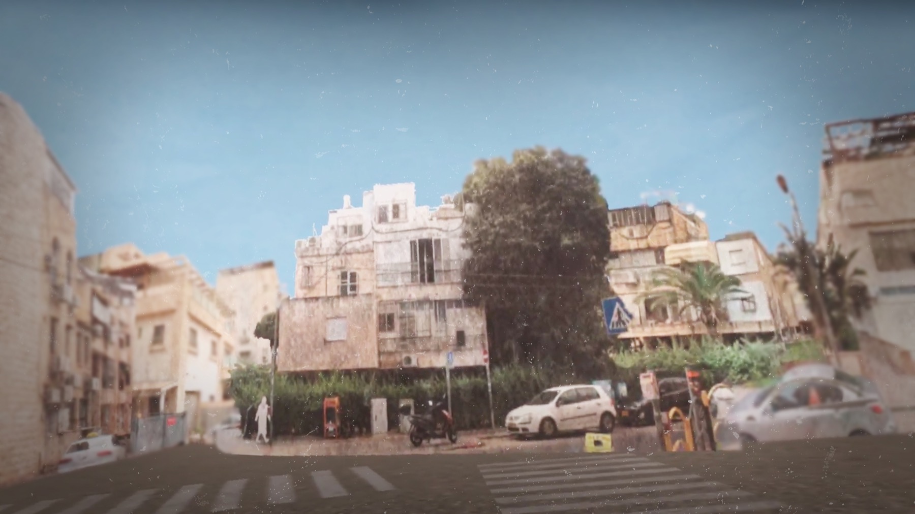 A residential street in Israel with white apartment buildings, parked cars and trees under a bright sky