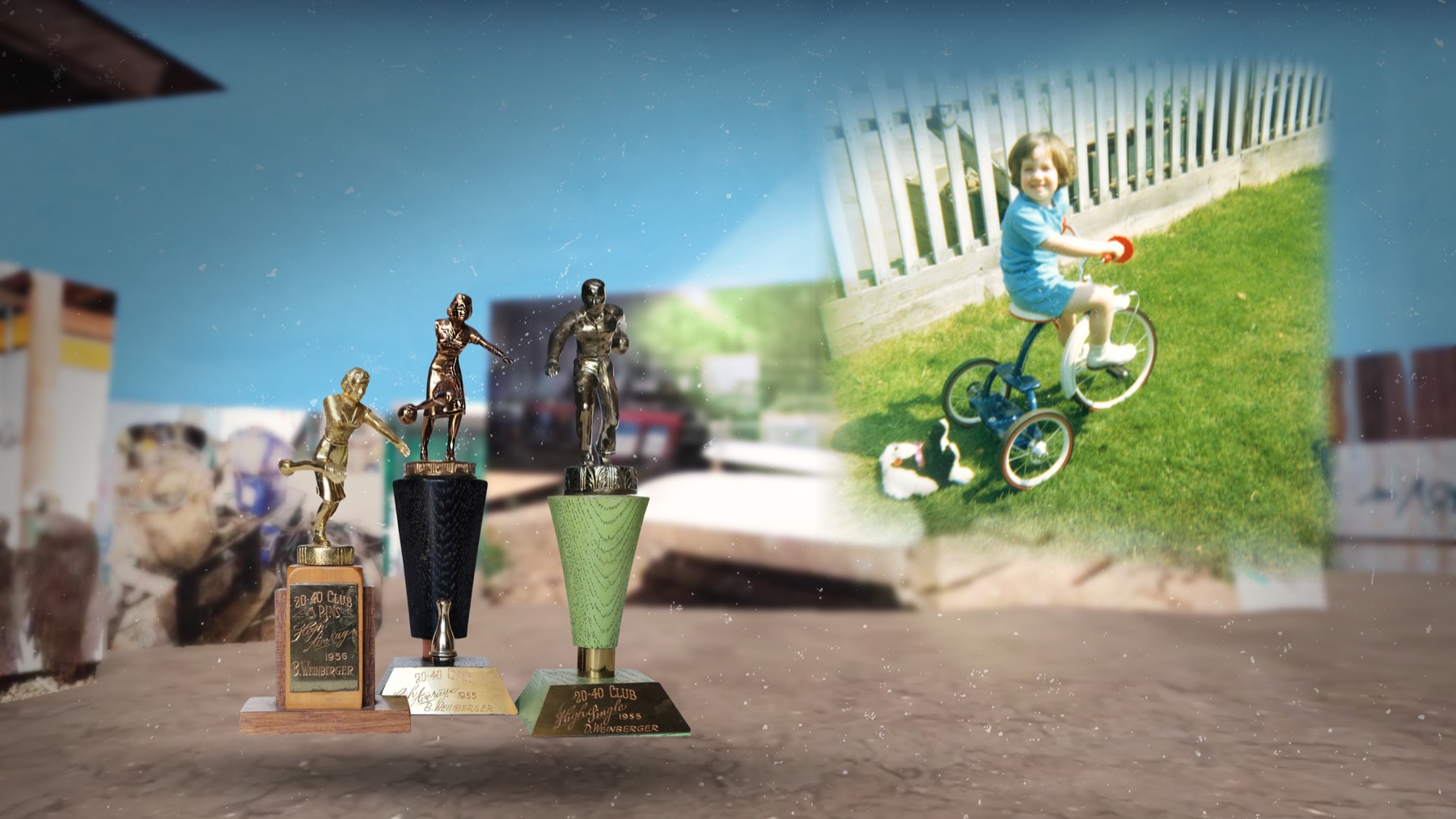 Three sports trophies standing in the salvage yard, with a projected image of a child riding a tricycle behind them