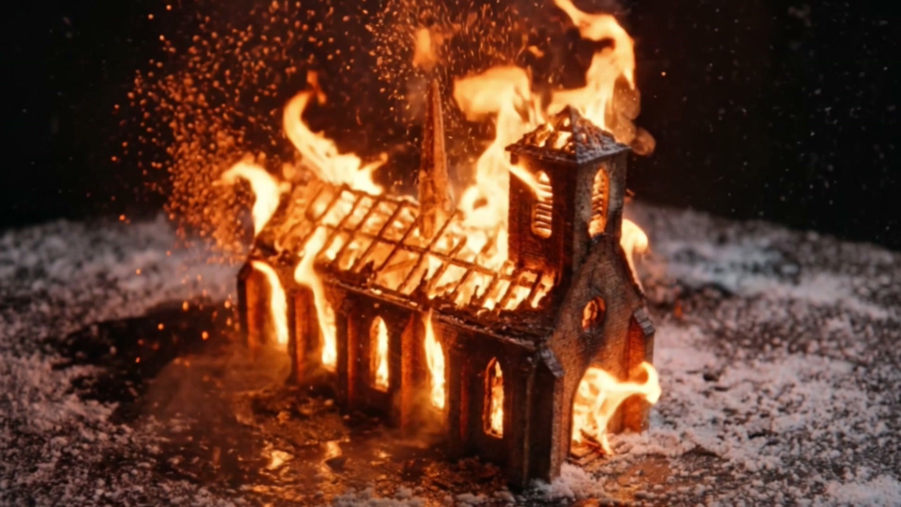 Film still: a model of a Gothic abbey church burning, saturated orange flames against deep indigo