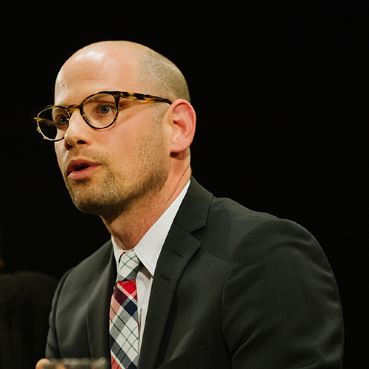 Photograph of Max Bergholz speaking, wearing round tortoiseshell glasses