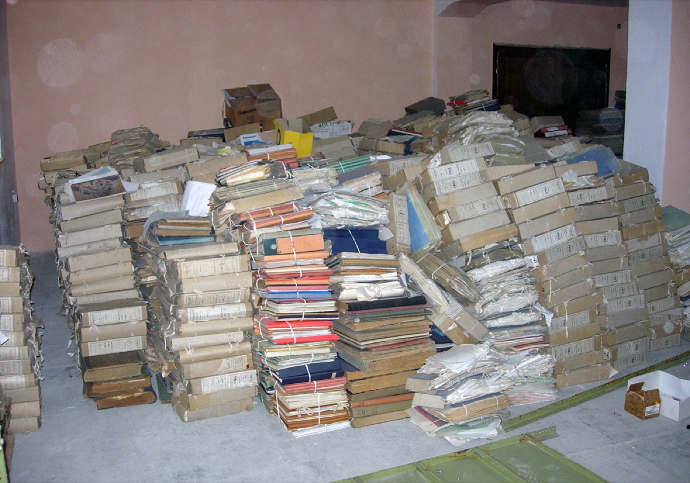 Photograph of a storage depot piled with bundled archival files, no shelving